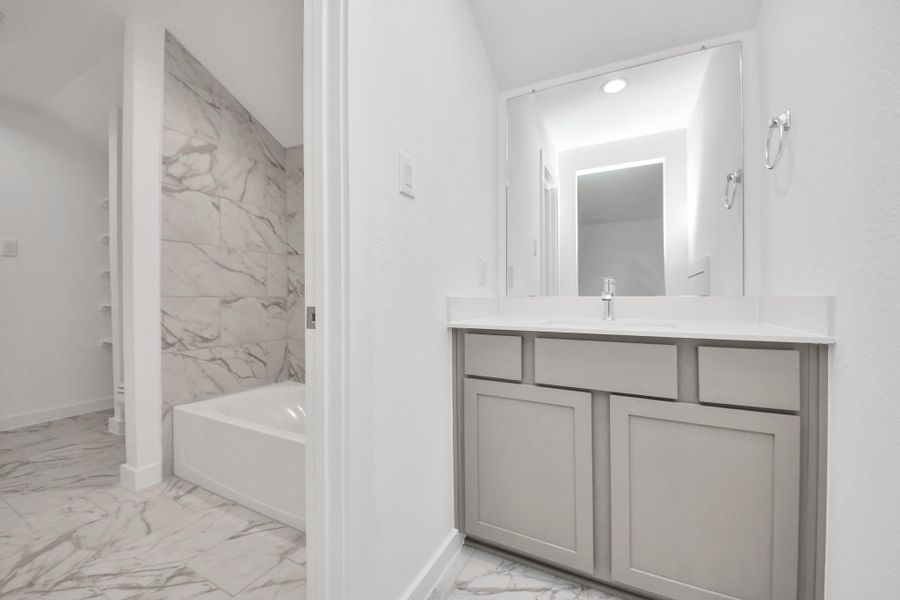 Experience convenience in the secondary bathroom, designed for Jack and Jill arrangements, now with a separate vanity area. This well-appointed space showcases stylish tile flooring, a bath/shower combo with an elegant tile surround, and light-stained wood cabinets. The beautiful light countertop adds a touch of sophistication, combining functionality and aesthetics seamlessly. Sample photo of completed home with similar floor plan. Actual colors and selections may vary.