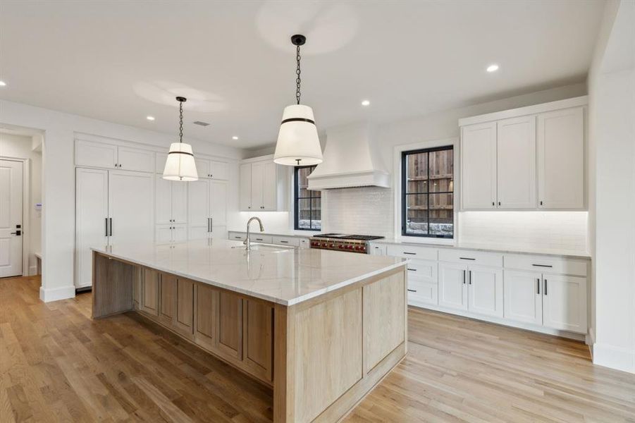 Kitchen featuring a large island, light stone counters, white cabinetry, custom exhaust hood, and light hardwood / wood-style flooring