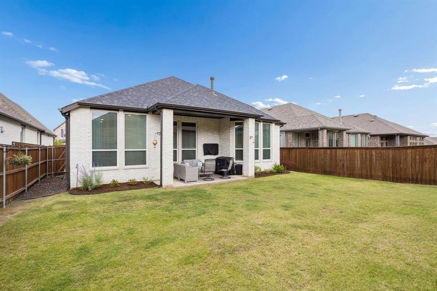 Expansive backyard featuring a manicured lawn, a full wooden privacy fence, and a covered patio with a concrete surface
