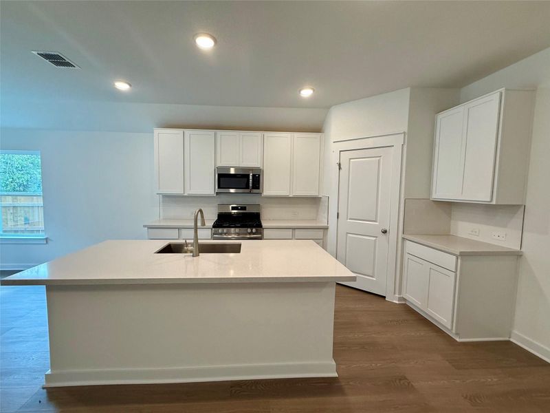 Kitchen featuring white cabinetry, dark wood-style flooring, stainless steel appliances, a kitchen island with sink, and recessed lighting Kitchen featuring white cabinetry, dark wood-style flooring, stainless steel appliances, a kitchen island with sink, and recessed lighting