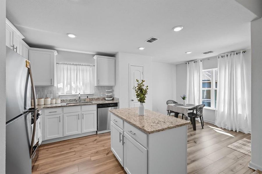 Kitchen featuring white cabinetry, appliances with stainless steel finishes, backsplash, light stone countertops, and light wood-type flooring