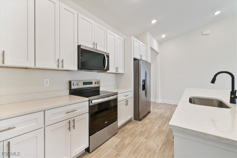 Kitchen featuring stainless steel appliances, light stone counters, white cabinets, wood tiled floors, and recessed lighting