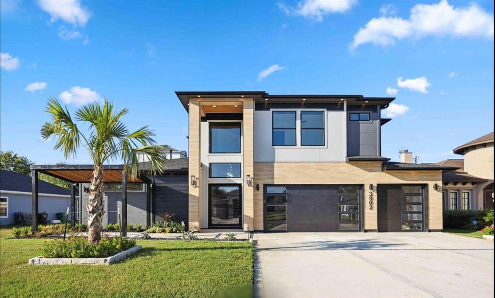 This is a modern two-story home featuring a mix of wood and stone facade, large windows, and a flat roof design. It has an attached two-car garage and is landscaped with a palm tree, giving it a warm, inviting look.