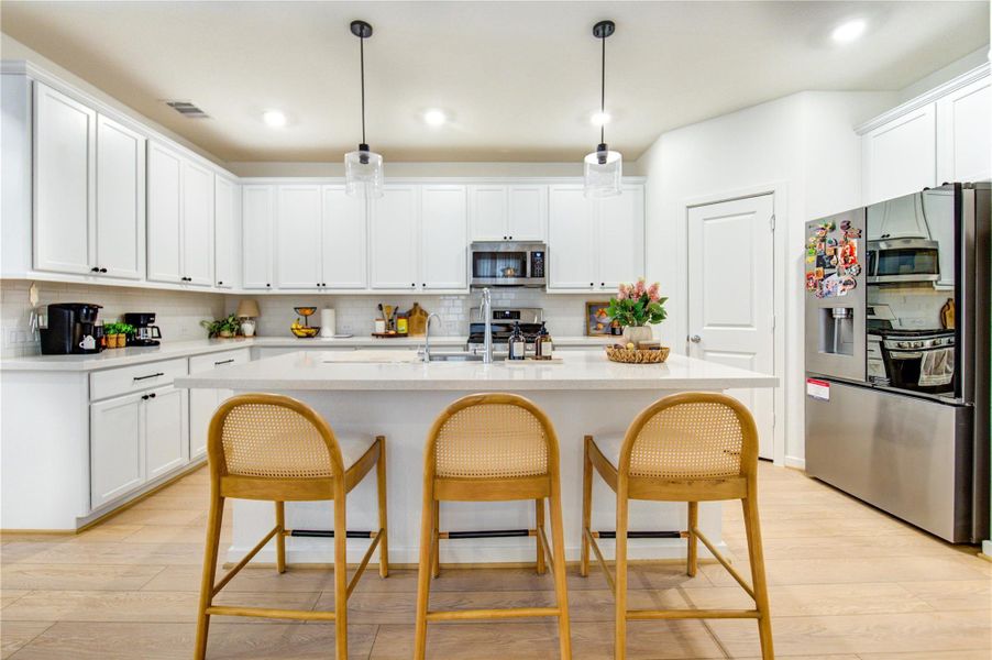 The gourmet kitchen showcases a generous breakfast bar that comfortably seats 3-4, providing an ideal space for both meal preparation and casual dining. Recessed and pendant lighting brighten the area, creating a warm and welcoming atmosphere for everyday living and entertaining. It also features a walk-in pantry, expansive quartz countertops, and abundant cabinetry with under-cabinet lighting for added convenience.