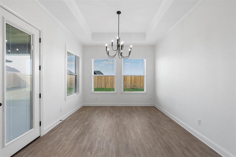 Unfurnished dining area with dark wood finished floors, crown molding, a chandelier, and a tray ceiling Unfurnished dining area with dark wood finished floors, crown molding, a chandelier, and a tray ceiling