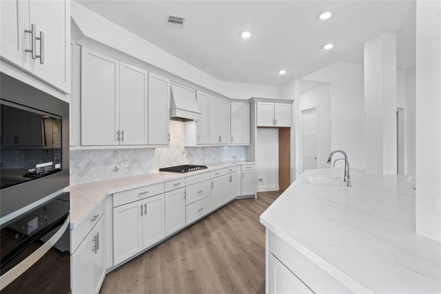 A sleek, built-in oven and microwave stack is seamlessly integrated into the cabinetry, complemented by a matching ventilation hood over the gas cooktop. A sleek, built-in oven and microwave stack is seamlessly integrated into the cabinetry, complemented by a matching ventilation hood over the gas cooktop.