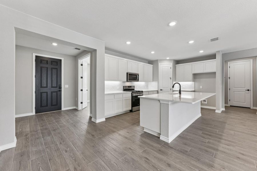 Kitchen with appliances with stainless steel finishes, recessed lighting, white cabinets, a kitchen island with sink, and light wood-style flooring Kitchen with appliances with stainless steel finishes, recessed lighting, white cabinets, a kitchen island with sink, and light wood-style flooring