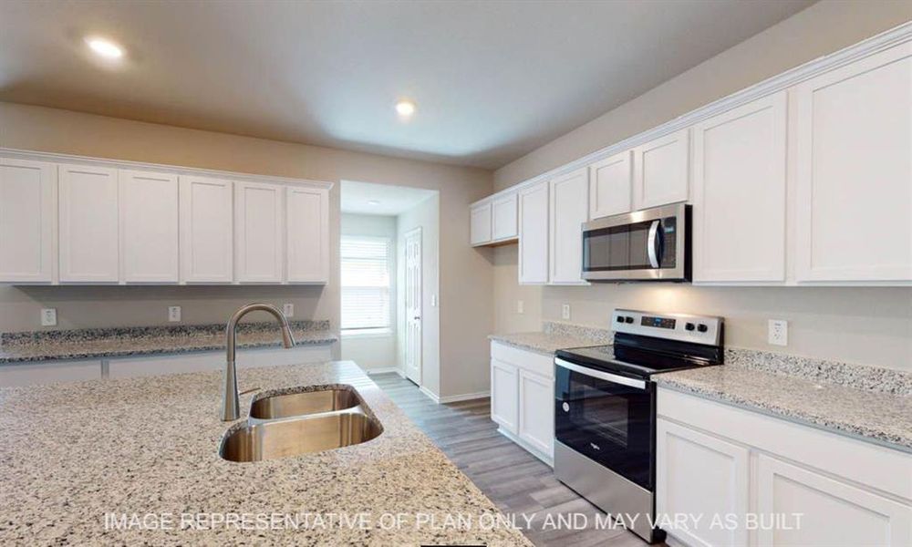 Spacious kitchen featuring an expansive island with an undermount double basin stainless steel sink, white shaker cabinetry, stainless steel appliances, speckled stone countertops, and wood-finish flooring Spacious kitchen featuring an expansive island with an undermount double basin stainless steel sink, white shaker cabinetry, stainless steel appliances, speckled stone countertops, and wood-finish flooring