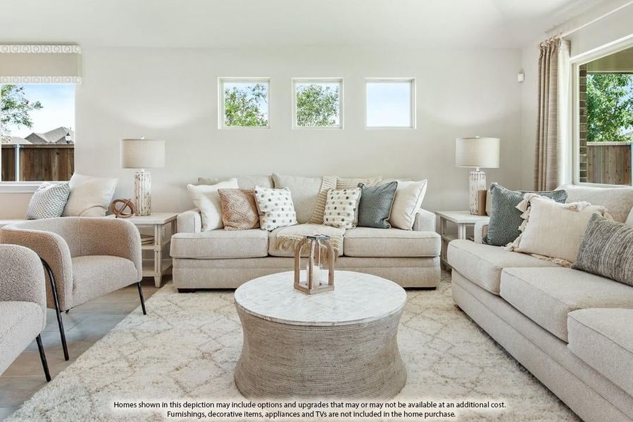 Bright living room with beige sofas, round coffee table, and three high windows letting in natural light