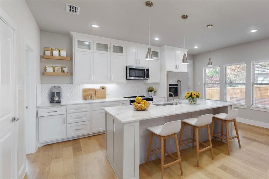 Virtual Staged Kitchen featuring pendant lighting, a center island with sink, white cabinetry, and appliances with stainless steel finishes