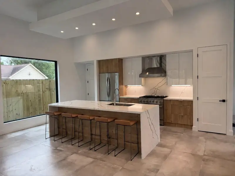 Sleek modern kitchen featuring a large waterfall island with low-maintenance quartz countertops, stainless steel appliances, and stylish wood cabinetry, illuminated by recessed lighting.