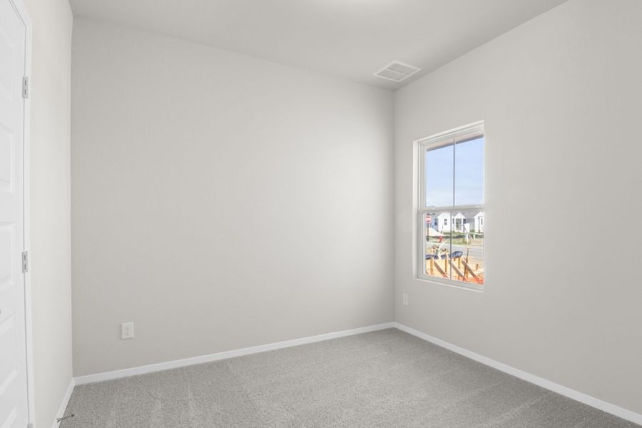 Image of a bedroom with tan carpeting, light grey walls and a window