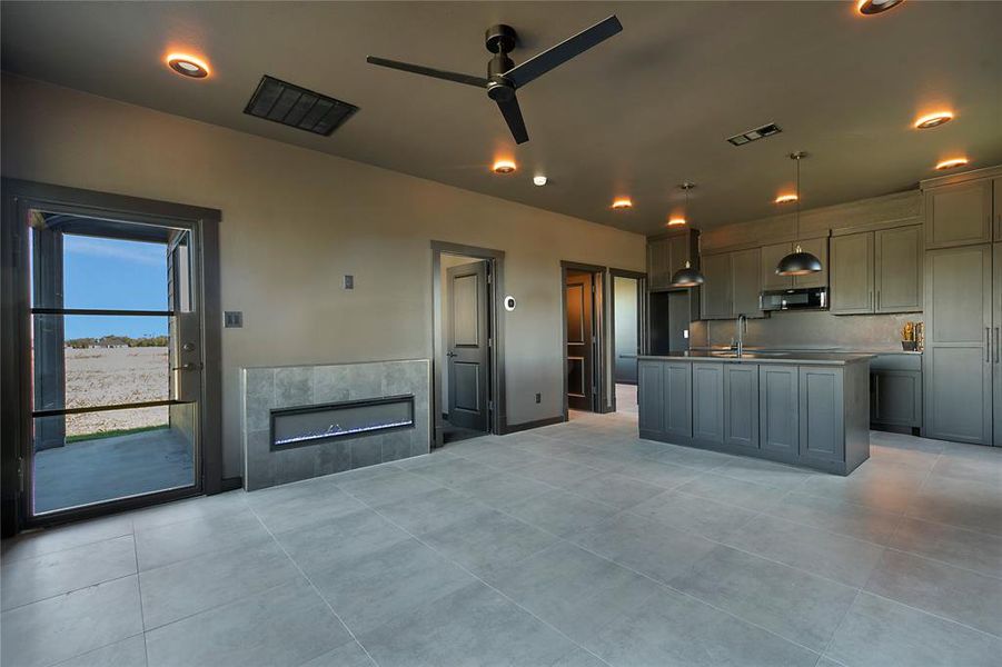 Kitchen featuring ceiling fan, a kitchen island with sink, a tile fireplace, black microwave, and gray cabinets Kitchen featuring ceiling fan, a kitchen island with sink, a tile fireplace, black microwave, and gray cabinets