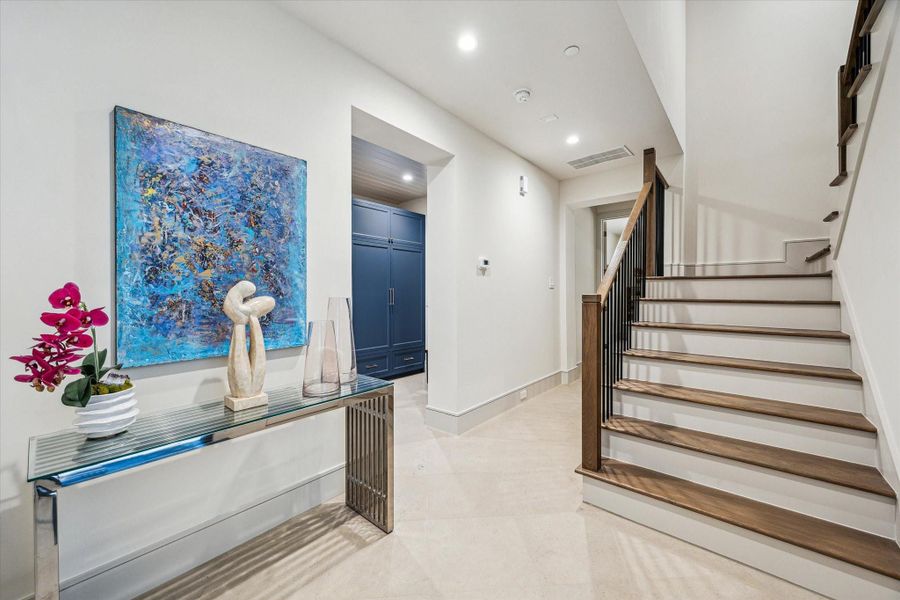 The hallway to the first floor bedroom shows off the large-format tile, deep baseboards, and stained oak stair treads.