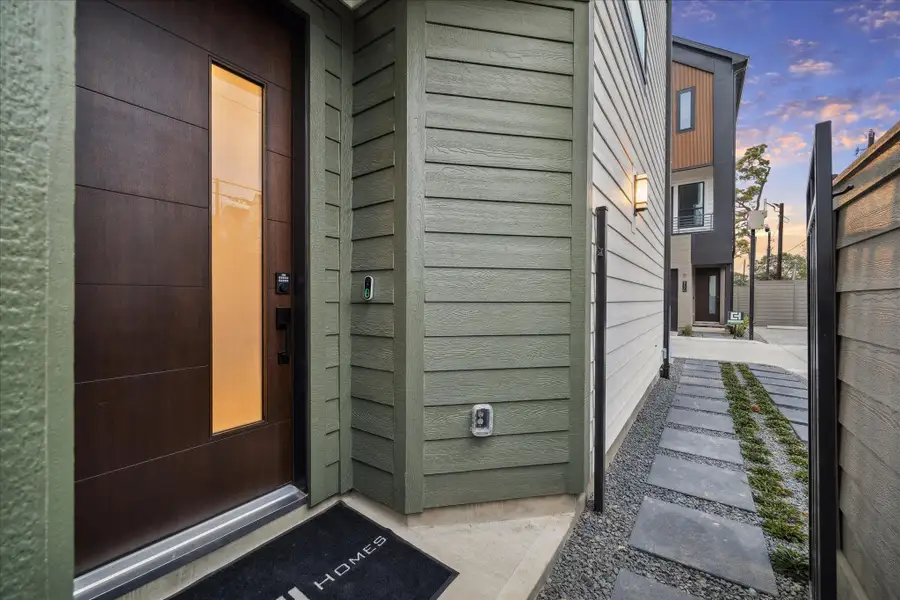 Modern entry makes a strong first impression with a sleek wood door, frosted glass panel, and clean horizontal siding. Stepping stone walkway and gated access add a private, thoughtfully designed approach.