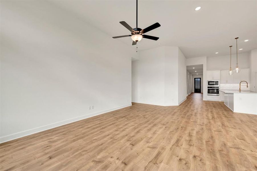 Spacious open-concept room featuring wood-finish flooring, a ceiling fan with light fixture, and white painted walls