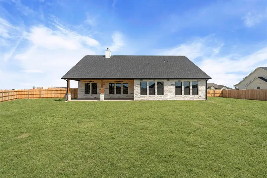 Rear view of house with a patio, a chimney, stone siding, a fenced backyard, and roof with shingles Rear view of house with a patio, a chimney, stone siding, a fenced backyard, and roof with shingles