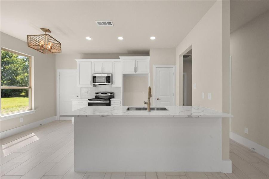 Kitchen with stainless steel appliances, white cabinets, sink, light stone counters, and backsplash