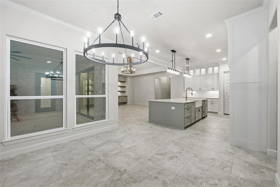 Kitchen with hanging light fixtures, an island with sink, white cabinets, decorative backsplash, and ornamental molding Kitchen with hanging light fixtures, an island with sink, white cabinets, decorative backsplash, and ornamental molding