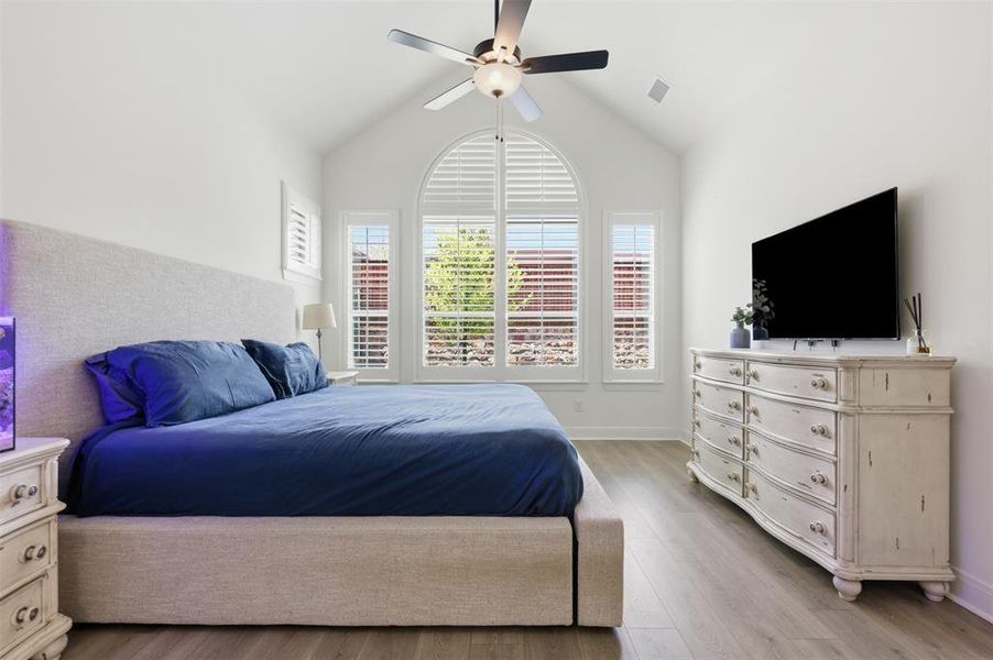 Vaulted ceiling room featuring wood-finish flooring, an arched window, a ceiling fan, and plantation shutters Vaulted ceiling room featuring wood-finish flooring, an arched window, a ceiling fan, and plantation shutters