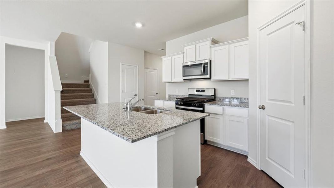 Kitchen with white cabinets, appliances with stainless steel finishes, an island with sink, light stone counters, and dark wood-style flooring