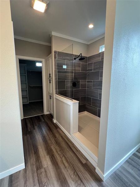 Bathroom with a textured wall, a spacious closet, walk in shower, dark wood-style floors, and crown molding