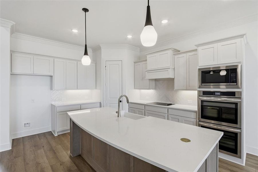 Kitchen featuring decorative backsplash, a center island with sink, dark wood-style floors, stainless steel appliances, and ornamental molding