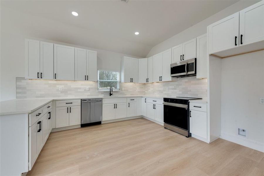 Kitchen with stainless steel appliances, white cabinetry, backsplash, and light hardwood / wood-style flooring