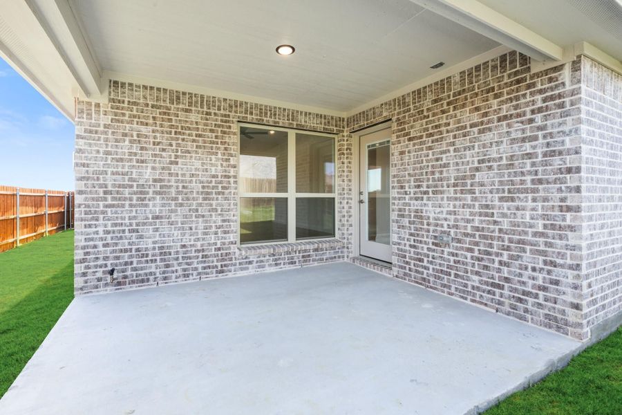 Covered back patio with concrete floor, brick exterior wall, and fenced backyard with green lawn