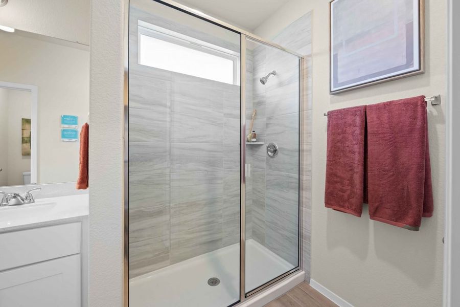 A interior image of a shower with a glass doow and red towels.
