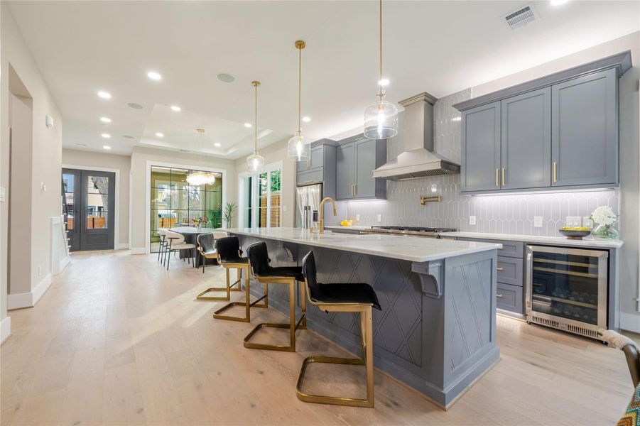 Kitchen with a breakfast bar, light wood-type flooring, tasteful backsplash, wine cooler, and pendant lighting