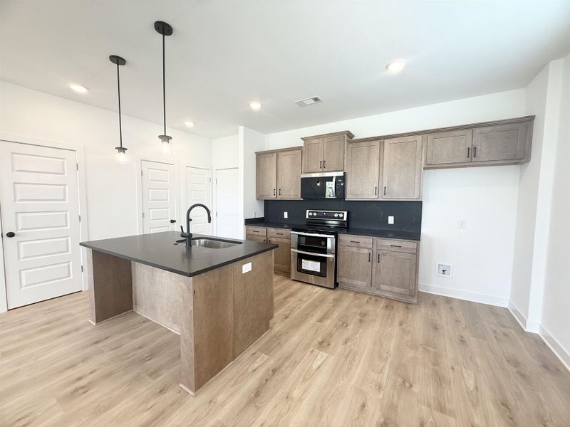 Kitchen with stainless steel appliances, dark countertops, light wood-type flooring, a center island with sink, and recessed lighting