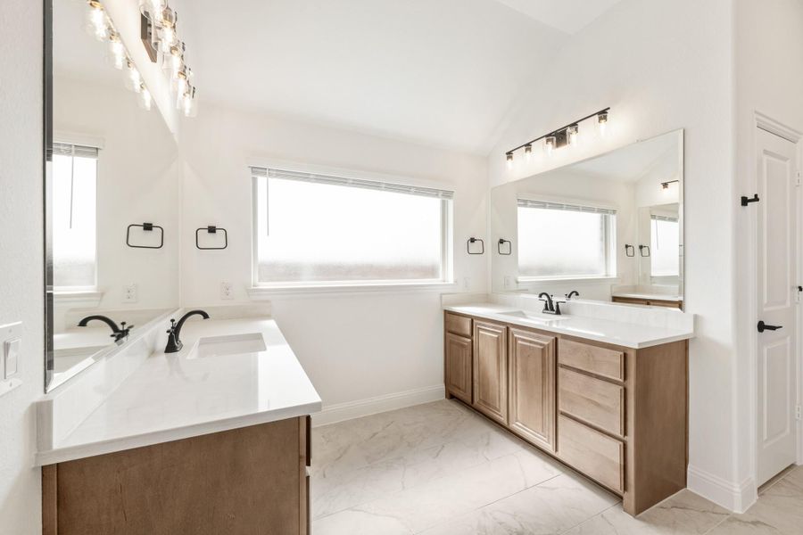 Dual-vanity bathroom with wood cabinets, white countertops, large mirrors, and marble tile floors
