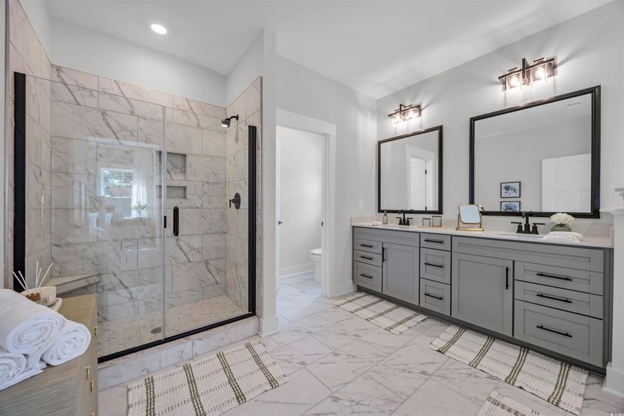Bathroom with light marble finish flooring, a marble finish shower, and double vanity