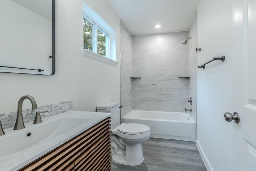 Modern bath with clean lines features a wood-slatted vanity and a full shower-tub combination. Modern bath with clean lines features a wood-slatted vanity and a full shower-tub combination.