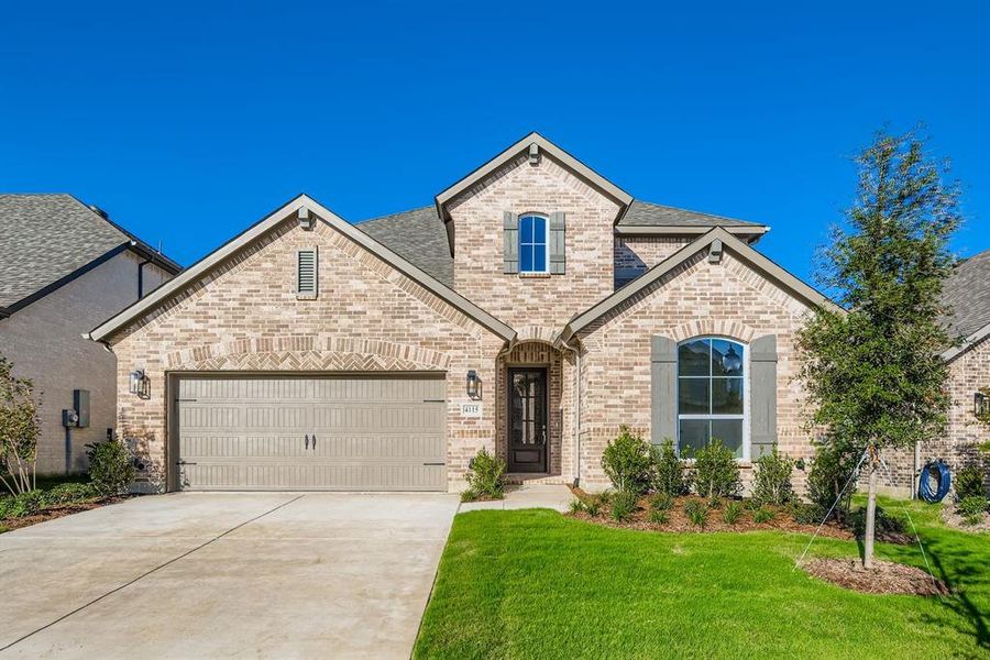 French country home with brick siding, concrete driveway, a garage, a front yard, and roof with shingles