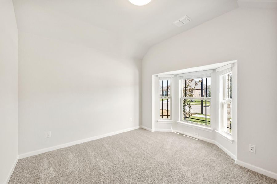 Empty bedroom with vaulted ceiling, carpet flooring, and a bay window overlooking a neighborhood