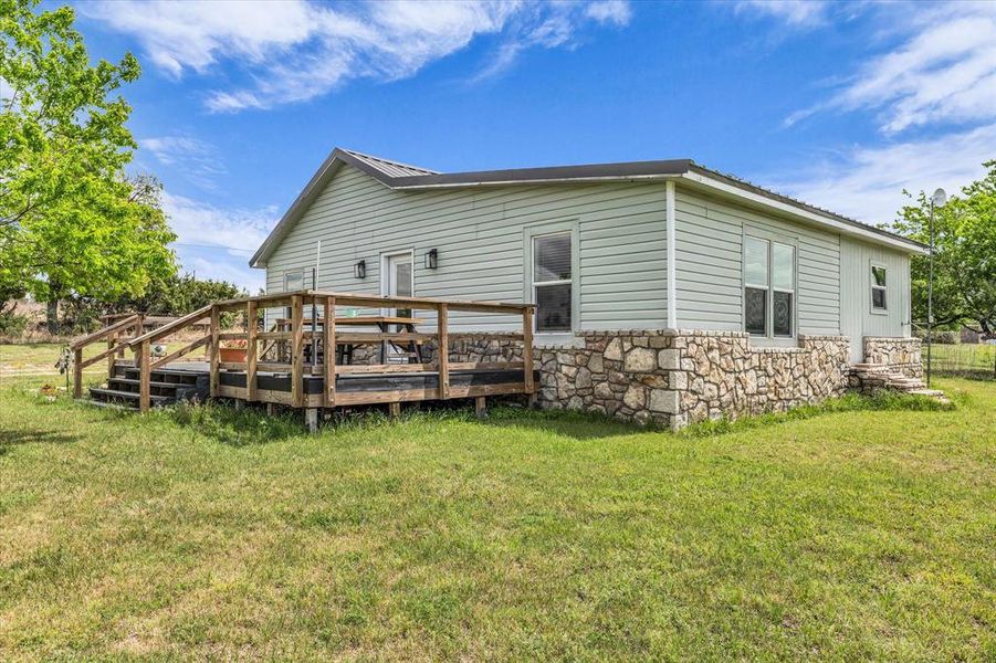 Back of house with stone siding, a lawn, and a wooden deck