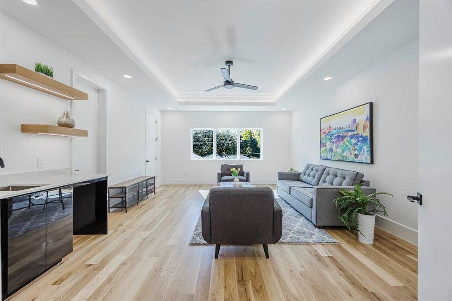 Living room with light wood-style floors, a ceiling fan, a tray ceiling, and recessed lighting Living room with light wood-style floors, a ceiling fan, a tray ceiling, and recessed lighting