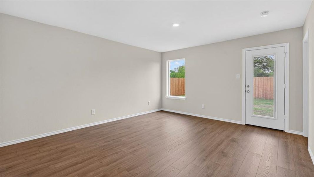 Spacious interior room featuring wood-finish flooring, light-toned walls, recessed ceiling lighting, a single window, and a glass-paneled exterior door Spacious interior room featuring wood-finish flooring, light-toned walls, recessed ceiling lighting, a single window, and a glass-paneled exterior door