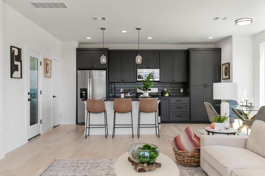 Kitchen featuring hanging light fixtures, backsplash, appliances with stainless steel finishes, a kitchen bar, and gray cabinets