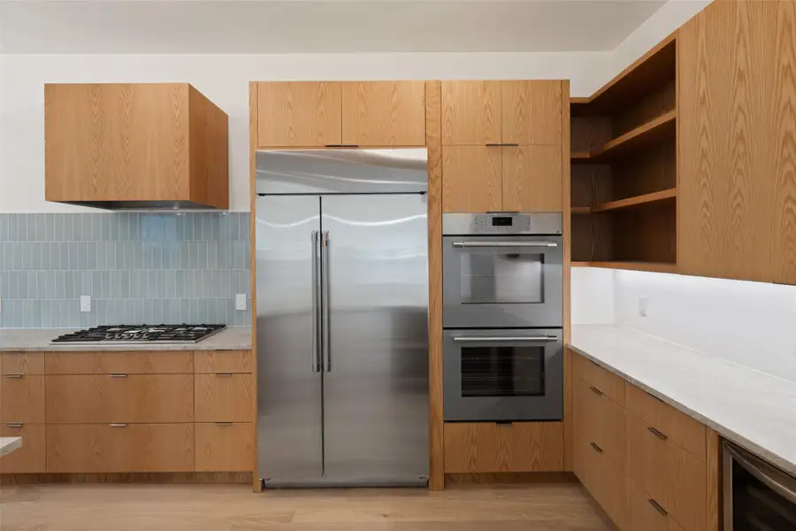 Kitchen featuring stainless steel appliances, modern cabinets, beverage cooler, light wood-style floors, and light stone countertops Kitchen featuring stainless steel appliances, modern cabinets, beverage cooler, light wood-style floors, and light stone countertops