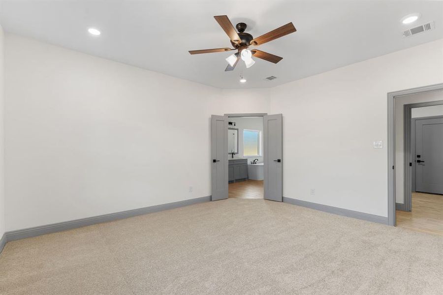 Unfurnished bedroom with light carpet, recessed lighting, ensuite bath, and a ceiling fan