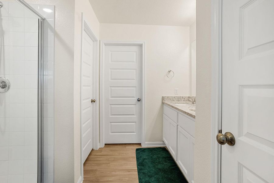 A well-lit bathroom features a white tiled shower and a vanity with granite counters.