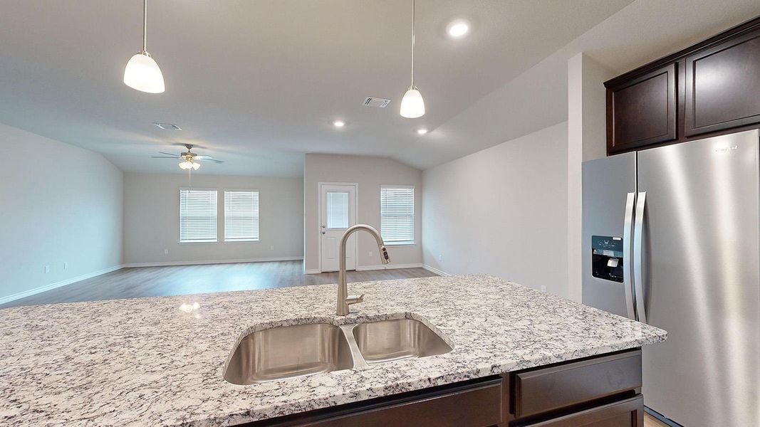 Kitchen with stainless steel fridge, dark wood finish cabinets, open floor plan, light stone counters, and vaulted ceiling