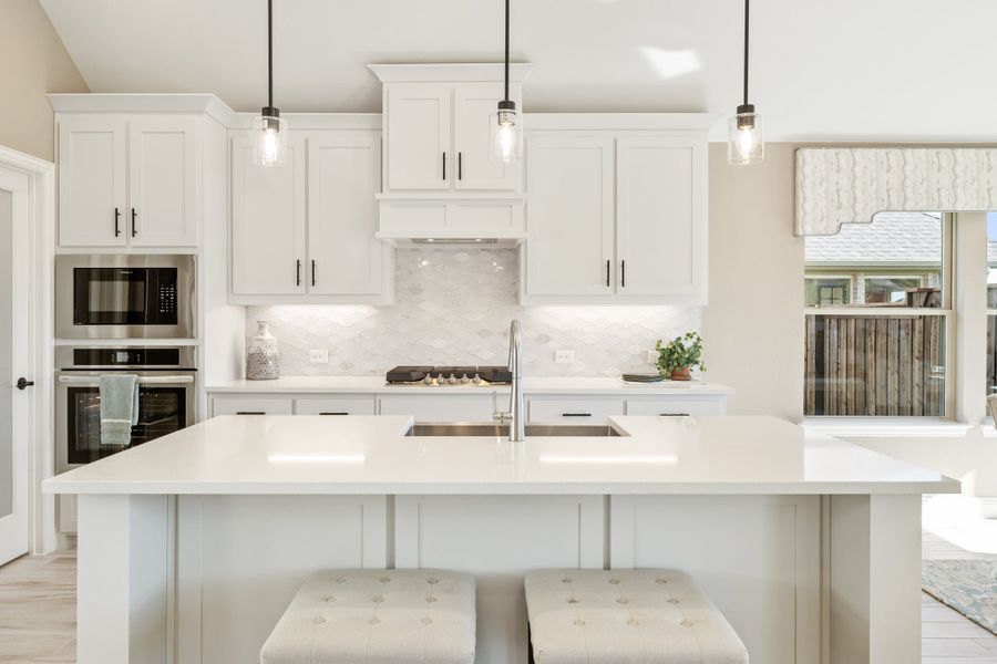 White kitchen with large island, pendant lights, stainless steel appliances, and marble backsplash