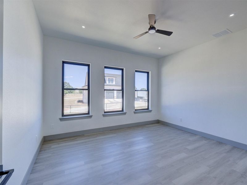 Three vertical windows fill this minimalist bedroom featuring durable hard-surface flooring.