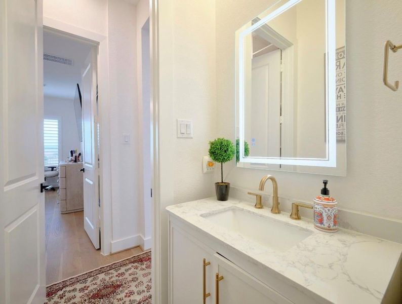 Stylish downstairs guest bath with quartz countertops and elegant mirrored lighting.