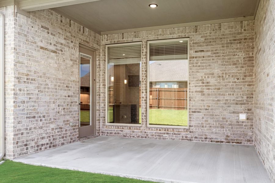 Covered back patio with concrete floor, light brick walls, and door leading to kitchen interior. Covered back patio with concrete floor, light brick walls, and door leading to kitchen interior.