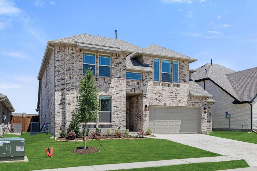 Two-story brick home with two-car garage, gray roof, and landscaped front yard